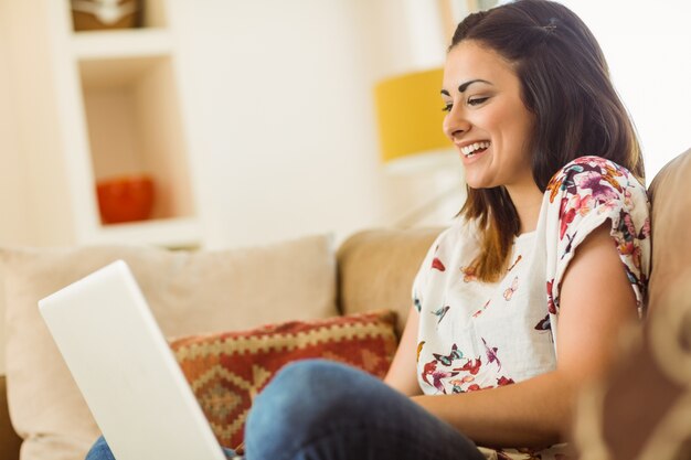 Hübscher Brunette, der auf Couch mit Laptop sich entspannt