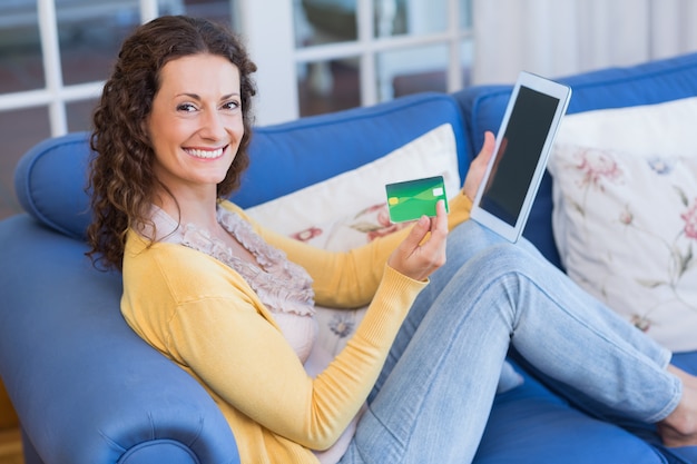 Hübscher Brunette, der auf der Couch mit Tablette sich entspannt