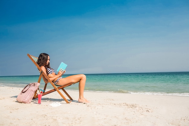 Hübscher Brunette, der ein Buch auf Klappstuhl liest