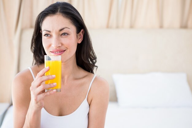 Hübscher Brunette, der ein Glas Orangensaft auf Bett hält