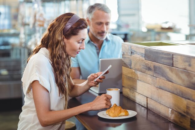 Hübscher Brunette, der ihren Smartphone mit Kaffee in ihrer Hand verwendet