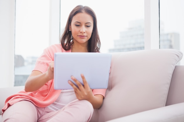 Hübscher Brunette, der ihren Tabletten-PC auf der Couch verwendet