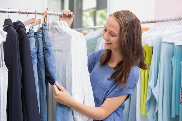 Hübscher Brunette, der im Kleiderständer durchstöbert