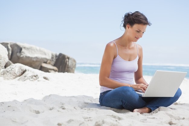 Hübscher Brunette, der Laptop auf dem Strand verwendet