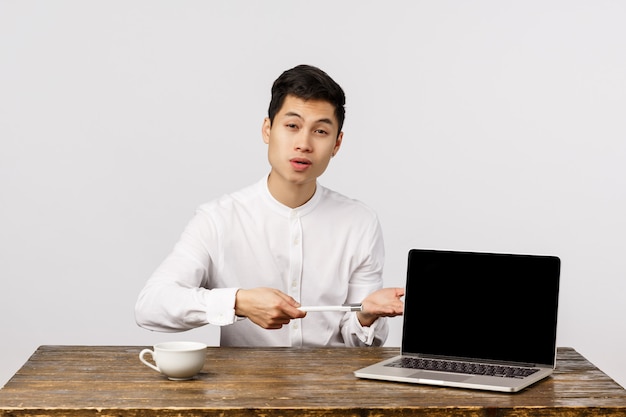 Hübscher chinesischer männlicher Manager, Büroangestellter stellen Kundenunternehmensprodukt vor, zeigen Diagramm auf Laptopschirm, zeigen Anzeige mit Stift und erklären das Konzept und sitzen