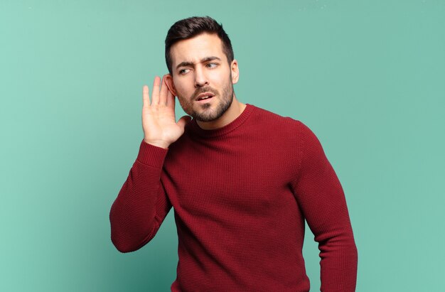 Hübscher erwachsener blonder Mann, der ernst und neugierig aussieht, zuhört, versucht, ein geheimes Gespräch oder einen Klatsch zu hören, zu lauschen