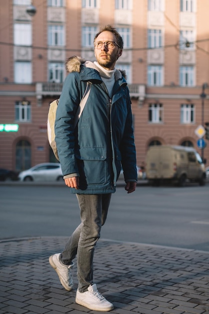 Hübscher erwachsener Mann in Jacke mit grünem Rucksack, der auf der Straße spazieren geht Tourist, der neue Stadt erkundet