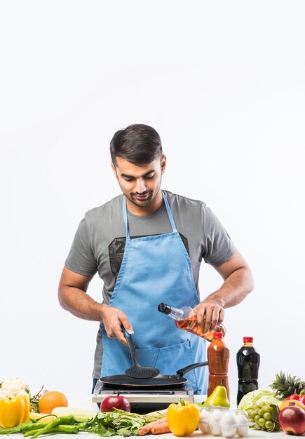 Hübscher, fröhlicher, lächelnder indischer Mann, der Essen in der Küche zubereitet, gesundes Essen, Kochkonzept.