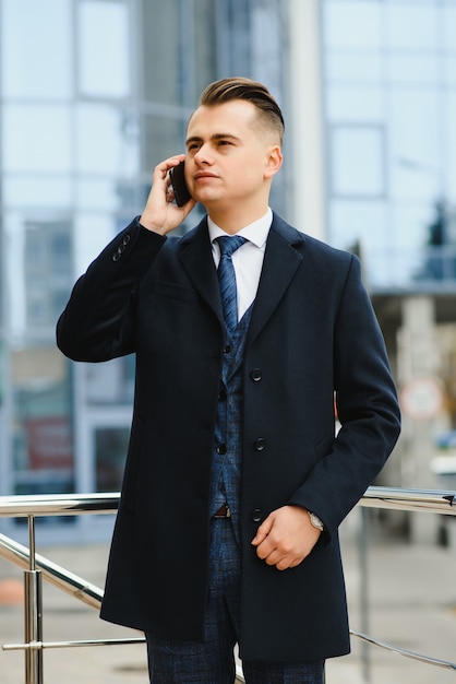 Hübscher Geschäftsmann, der durch Bürogebäude steht, das Geschäftsanruf auf Mobiltelefon hat