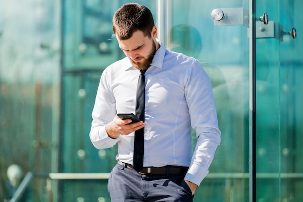 Hübscher Geschäftsmann, der durch Mobiltelefon simst