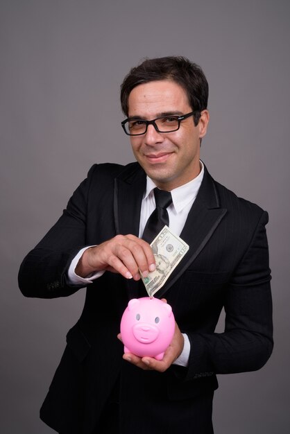 Hübscher Geschäftsmann, der Geld in Sparschwein einfügt