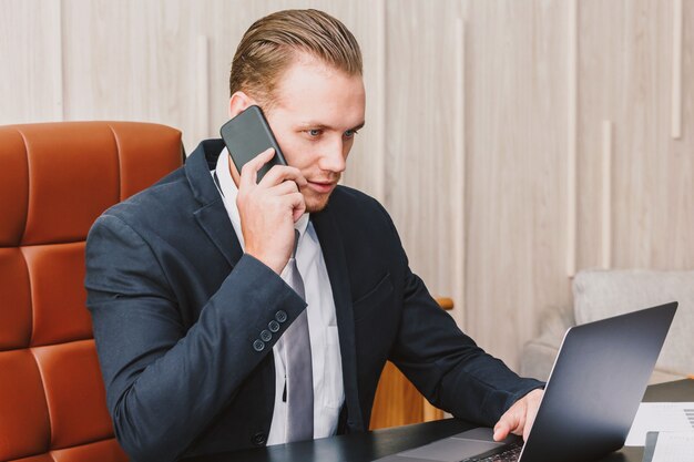 Hübscher Geschäftsmann, der seinen Smartphone verwendet und an Notebook im Büro arbeitet