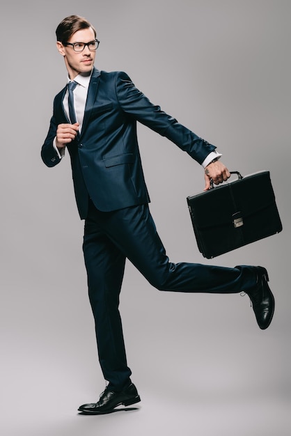 Hübscher Geschäftsmann im Anzug, der mit Aktenkoffer auf grauem Hintergrund läuft
