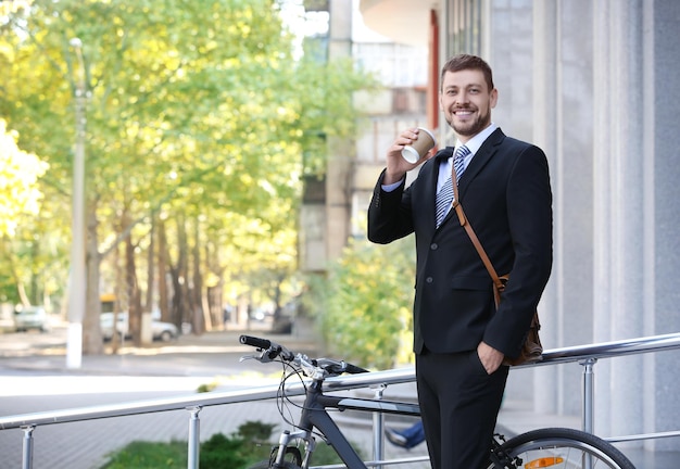 Hübscher Geschäftsmann mit seinem Fahrrad, der draußen Kaffee trinkt