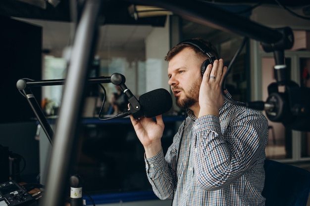 Hübscher, glücklicher junger männlicher Radiomoderator, der im Studio mit Mikrofon und Kopfhörern sendet