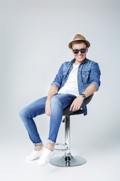 Hübscher glücklicher Mann in Jeans und Sonnenbrille sitzt auf Stuhl