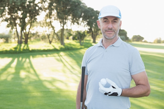 Hübscher Golfspieler, der mit Golfball steht