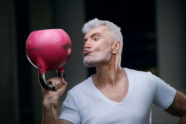 Hübscher grauhaariger älterer Mann mit rosa Kettlebellgewicht. Sport- und Gesundheitskonzept