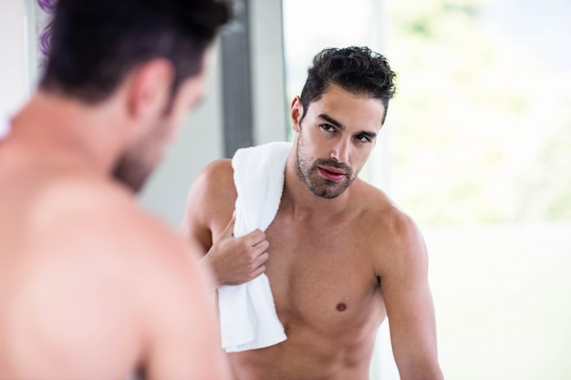 Hübscher hemdloser Mann, der im Spiegel im Badezimmer schaut