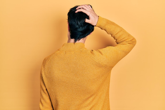 Hübscher Hipster-Junger, der einen lässigen gelben Pullover trägt und rückwärts über Zweifel mit der Hand auf dem Kopf nachdenkt