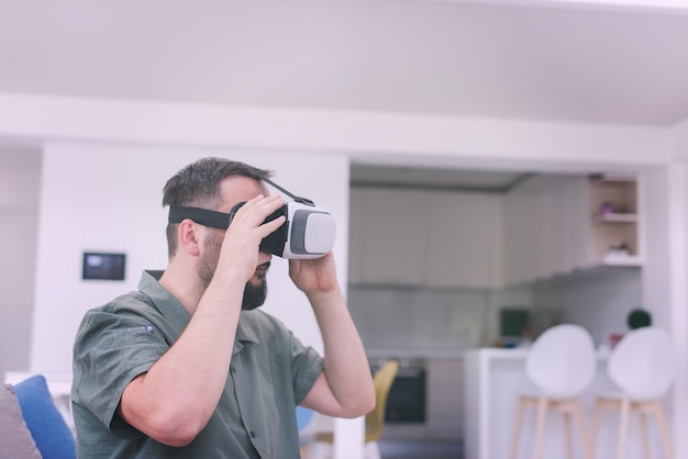 hübscher Hipster-Mann mit Bart, der eine VR-Brille im modernen Zuhause versucht