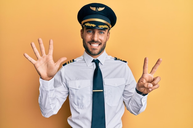 Hübscher hispanischer Mann in Flugzeugpilotenuniform, der mit den Fingern Nummer sieben nach oben zeigt und dabei selbstbewusst und glücklich lächelt