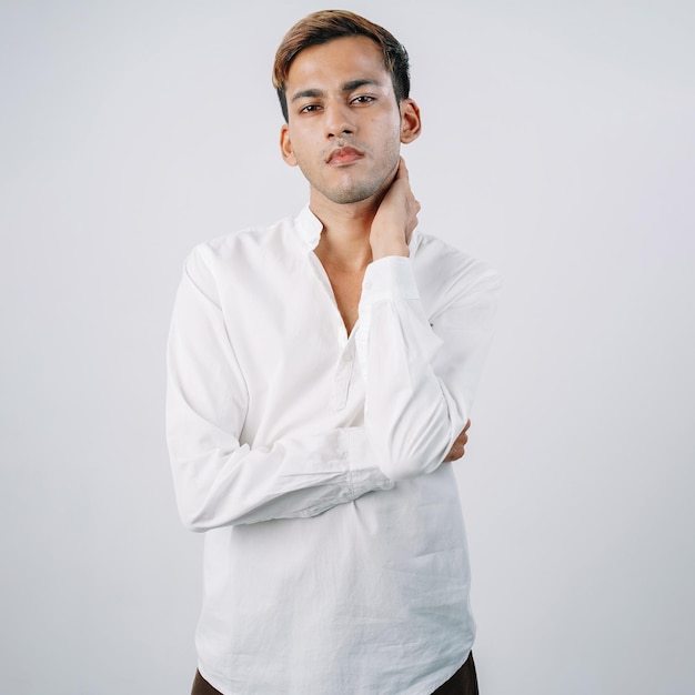 Hübscher indischer junger Geschäftsmann, der den Hals stehend isolierte graue Wand berührt