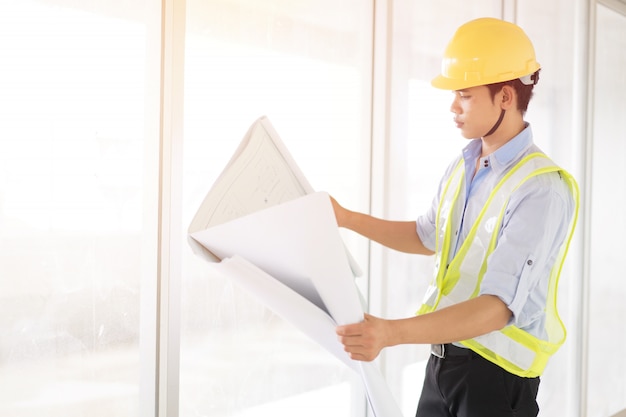 Hübscher Ingenieur, der Plan hält und im Büro lächelt.