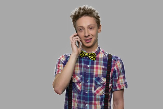 Hübscher jugendlich Junge, der auf Handy spricht. Stilvoller Teenager, der auf Handy gegen grauen Hintergrund spricht.