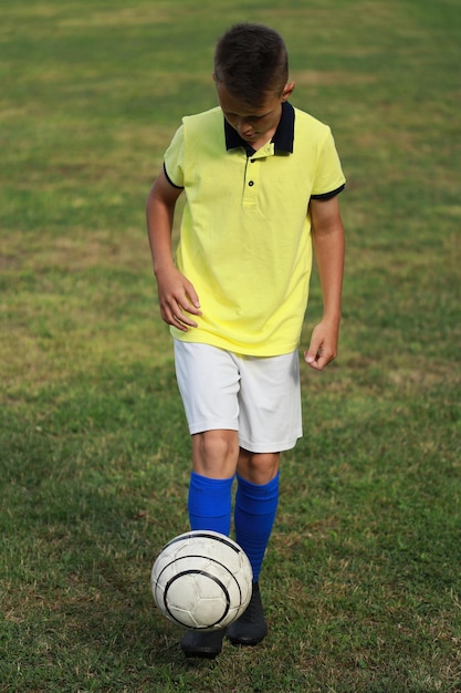 Hübscher Junge Fußballspieler in einem gelben T-Shirt auf dem Fußballplatz jongliert den Ball