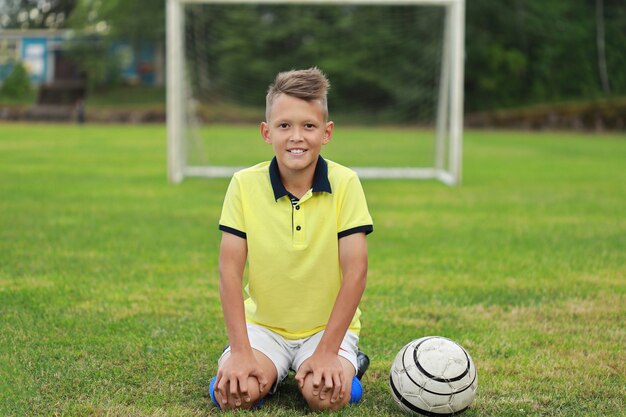 Hübscher Junge Fußballspieler in einem gelben T-Shirt sitzt auf dem Fußballplatz