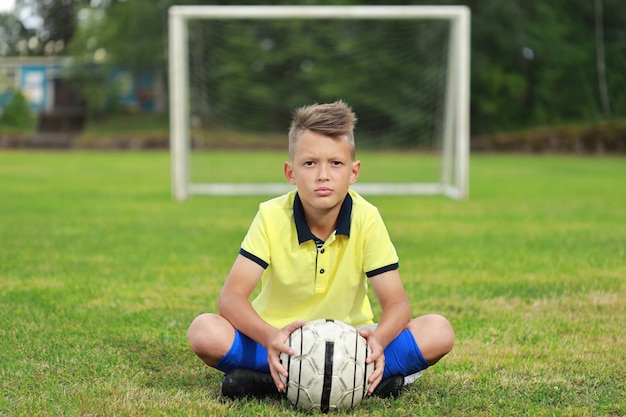 Foto hübscher junge fußballspieler in einem gelben t-shirt und blauem gntra sitzt auf dem fußballplatz