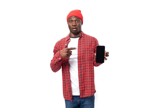 Hübscher junger amerikanischer Mann mit roter Kopfbedeckung, der Werbung auf Smafton mit Attrappe auf isoliertem Hintergrund zeigt
