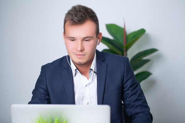 Hübscher junger Arbeiter, der in einem Firmenbüro mit Dokumenten und einem Laptop arbeitet