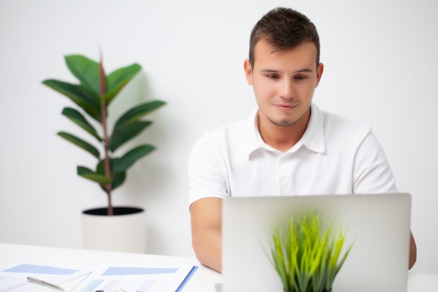 Hübscher junger Arbeiter, der in einem Firmenbüro mit Dokumenten und einem Laptop arbeitet