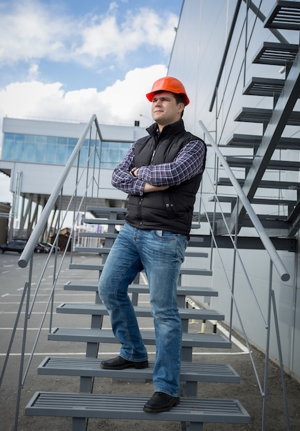 Hübscher junger Architekt mit Schutzhelm posiert auf Metalltreppe