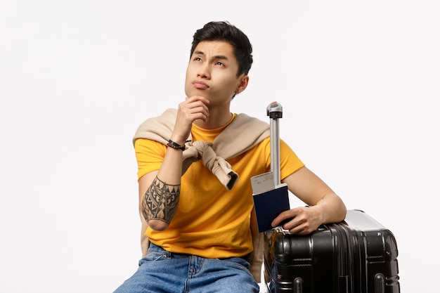 Hübscher junger asiatischer mann im gelben t-shirt bereit, mit rollkoffer und pass zu reisen