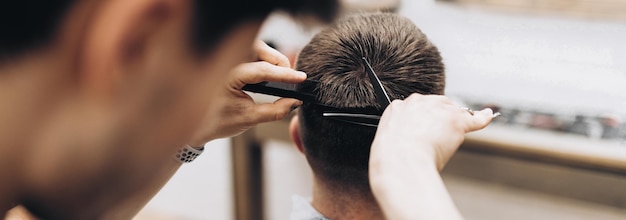 hübscher junger bärtiger kerl, der in einem sessel in einem schönheitssalon sitzt und der friseur in seiner nähe