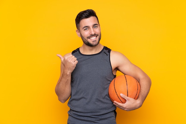 Hübscher junger Basketball-Spielermann über lokalisierter weißer Wand zeigend auf die Seite, um ein Produkt darzustellen