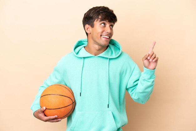 Hübscher junger Basketballspieler, isoliert auf ockerfarbenem Hintergrund, der auf eine großartige Idee zeigt
