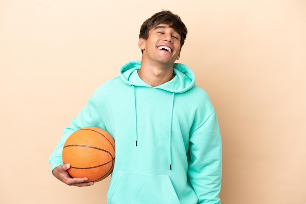 Hübscher junger Basketballspieler Mann isoliert auf ockerfarbenem Hintergrund lachend