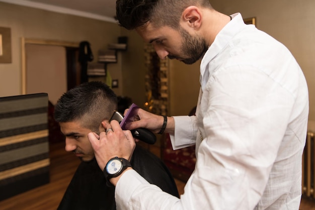 Hübscher junger Friseur, der männlichen Kunden im Salon einen neuen Haarschnitt gibt