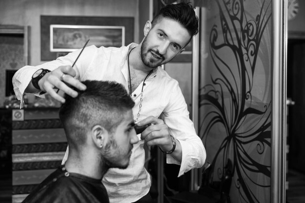 Hübscher junger friseur, der männlichen kunden im salon einen neuen haarschnitt gibt