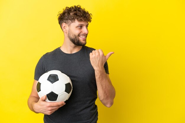 Hübscher junger Fußballspielermann einzeln auf gelbem Hintergrund, der auf die Seite zeigt, um ein Produkt zu präsentieren