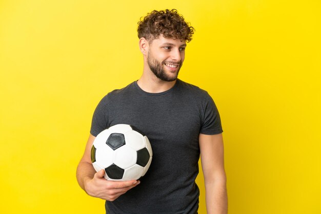 Hübscher junger Fußballspielermann lokalisiert auf gelbem Hintergrund, der zur Seite schaut und lächelt