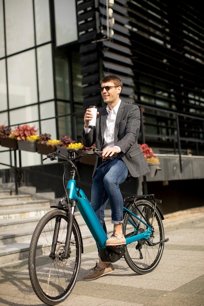 Hübscher junger Geschäftsmann auf dem E-Bike mit Kaffeetasse zum Mitnehmen