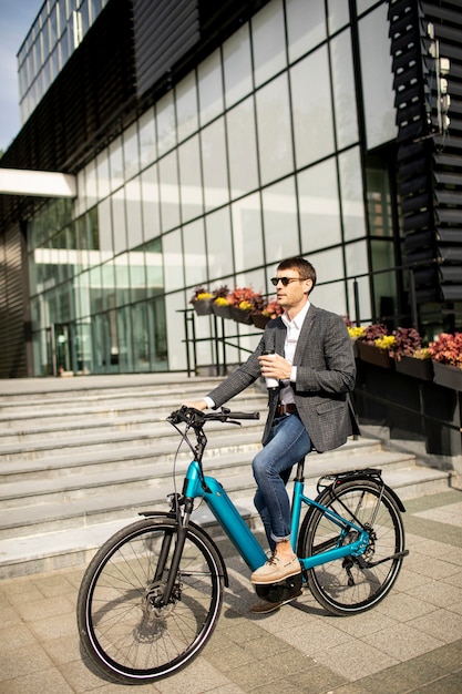 Hübscher junger Geschäftsmann auf dem E-Bike mit Kaffeetasse zum Mitnehmen