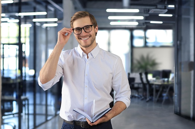 Hübscher junger Geschäftsmann, der im modernen Büro steht