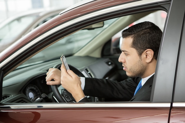 Foto hübscher junger geschäftsmann, der sein telefon benutzt, das in einem auto sitzt