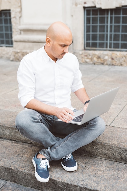 Hübscher junger Geschäftsmann in einem weißen Hemd, das mit einem Laptop arbeitet